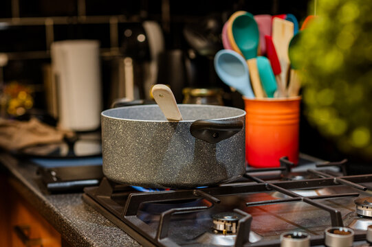 Simmering pot on gas stove with colorful kitchen utensils