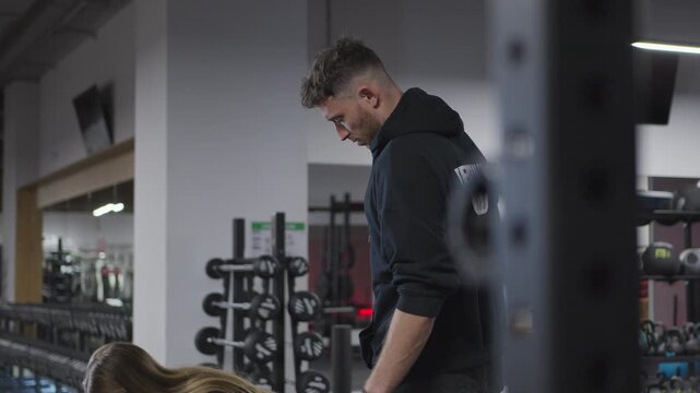Male personal trainer reviews a workout on a tablet, coaches a woman through a barbell Romanian deadlift, then celebrates with a high five in slow motion.