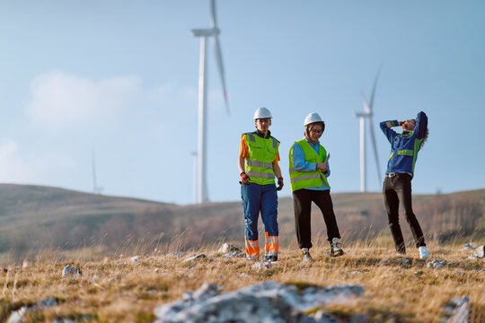 Wind Farm Engineers Inspecting Turbines on Grassy Hill in High-Visibility Safety Gear