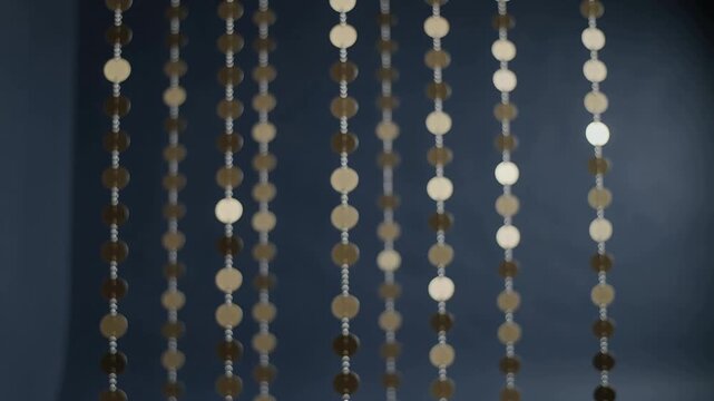 Swaying beaded curtain shifting strings and moving disc gleaming at blue-gray wall, light in breeze