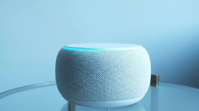 A modern smart speaker sits on a glass table, its light blue ring glowing softly as it processes a request. The minimalist environment and clean lighting emphasize its sleek design.