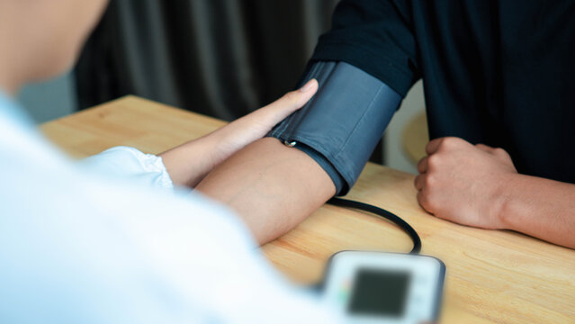 Healthcare worker measures a patient's blood pressure with an arm cuff in a clinic. Concept of cardiovascular screening, hypertension monitoring, medical checkup, prevention, and routine health care.