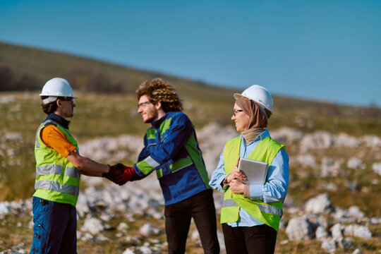 Construction Workers Shaking Hands On Site With Female Engineer Wearing Hijab And Safety Gear
