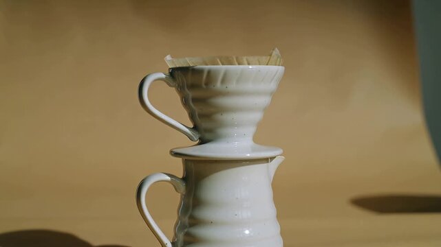 Bringing hands from left lowering dripper with paper filter onto pitcher on table, prepping coffee