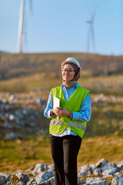 Female Engineer in Safety Vest and Hard Hat Inspecting Wind Turbines on Wind Farm