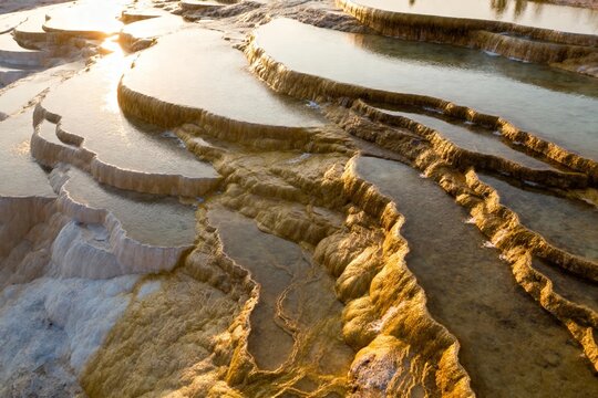 Sunlit travertine terraces with mineral-rich pools and golden-hued formations