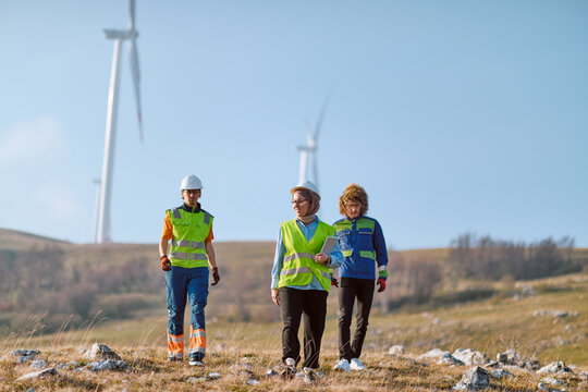 Renewable Energy Engineers Inspect Wind Turbines On Wind Farm Wearing Safety Vests And Hard Hats