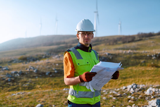 Field Engineer at Wind Farm Reviewing Construction Plans for Renewable Energy Project in Rural Landscape
