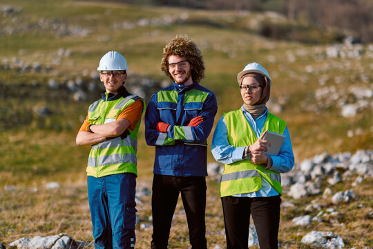 Construction Engineers and Surveyors Wearing Hard Hats and Hi-Vis Vests on Rural Site Showing Teamwork