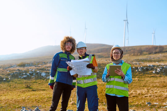 Engineers Inspecting Wind Farm Turbines With Blueprints and Tablet &mdash; Renewable Energy Team