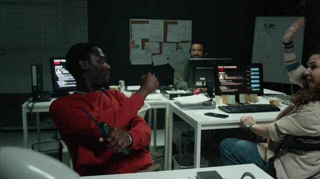 African American young man talking on radio transceiver and celebrating success with Caucasian colleague conducting fraud in office. Suitable for cybersecurity and scam awareness