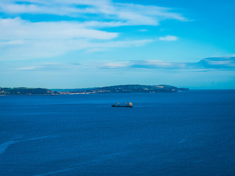 Aerial view of a cargo ship sailing on the calm blue waters of the Irish Sea near the coastline, with rolling green hills, Bangor, Northern Ireland, United Kingdom.
