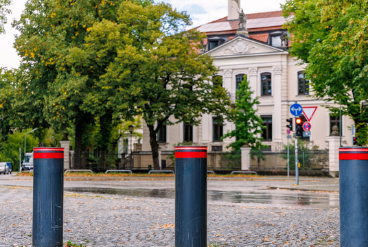 Three black retractable security bollards with red LED lights on wet cobblestone street in front of a historic building, urban safety, access control and traffic barrier concept