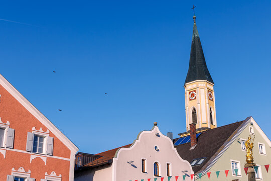 Colorful historic townhouses with baroque gables and church tower with clock against blue sky in the old town of Kelheim, Lower Bavaria, Germany, bunting flags, copy space