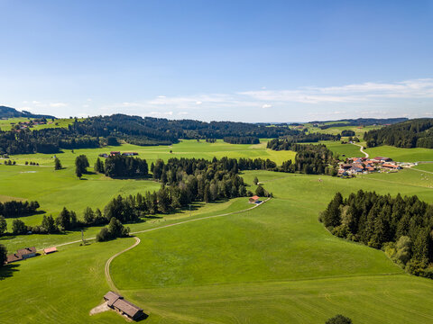 Aerial view of green meadows, forests and Bavarian farmhouses under blue sky near Bernbeuren, Upper Bavaria, Germany, idyllic rural landscape in summer