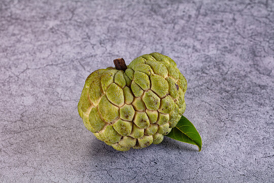 Fresh green custard apple with attached leaf on textured gray surface