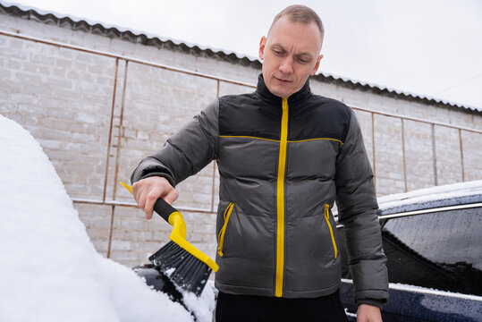 Man remove snow from vehicle in cold winter weather