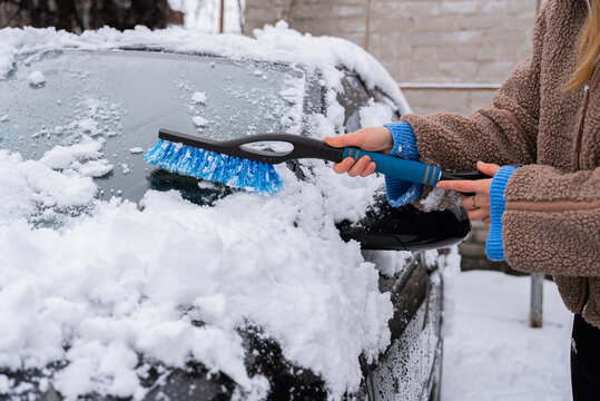 Woman remove snow from car windshield with brush