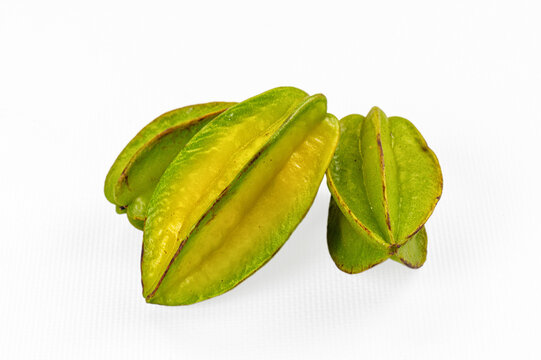 White textured surface with three green yellow star fruits showing ribbed skin and natural blemishes