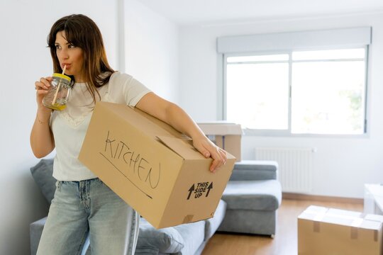 Woman carry moving box and drink in new apartment