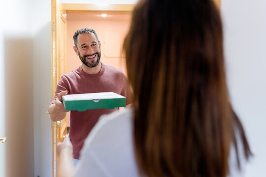 Smiling man surprise woman with pizza box at home