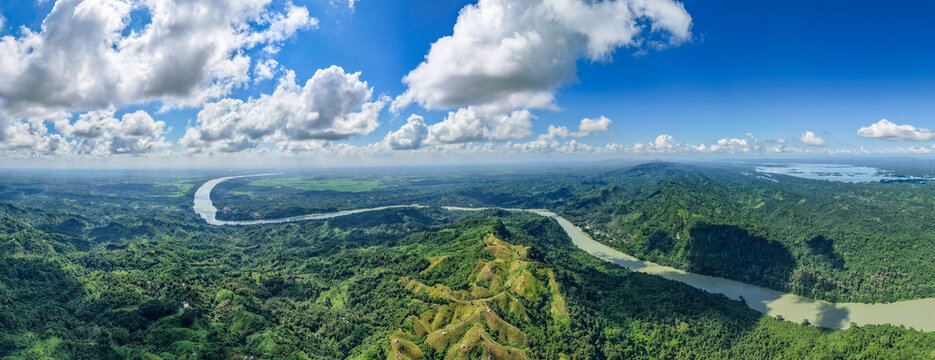 Aerial view of Shita Pahar featuring lush green hills, the winding Karnaphuli River, and a bright blue sky with scattered white clouds in Kaptai, Chittagong Division, Bangladesh.