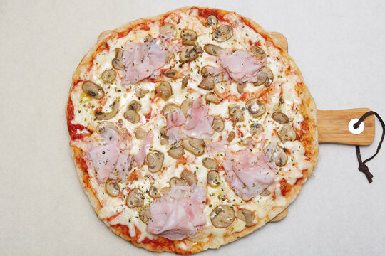 Italian ham and mushroom pizza on wooden serving paddle
