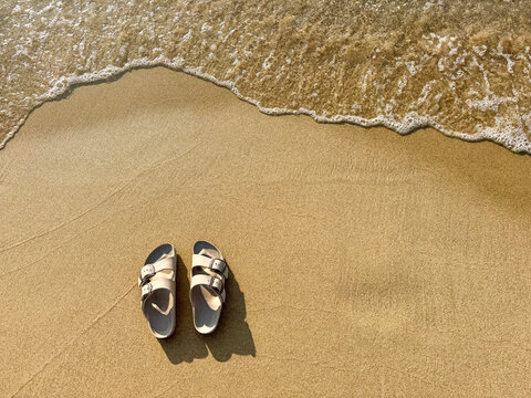 Sandals on sandy beach beside gentle sea wave