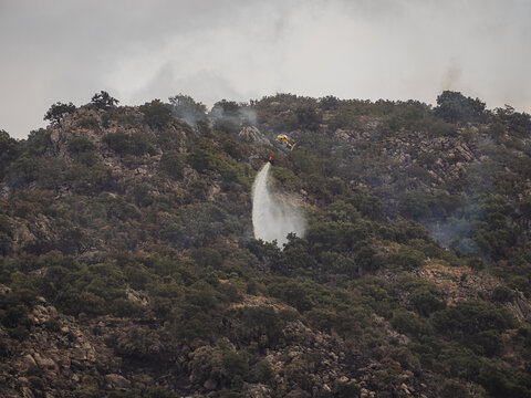 Firefighting helicopter drop water on rocky wildfire hillside