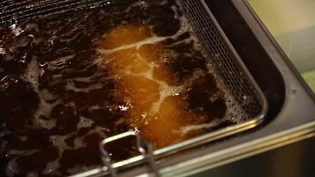 Tempura sushi roll fries in bubbling hot oil inside a commercial deep