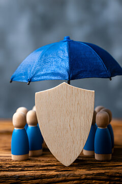 Family life insurance, healthcare protection, and a protective shield with wooden figures and a peg doll on a table for child safety, domestic welfare, and a health policy.
