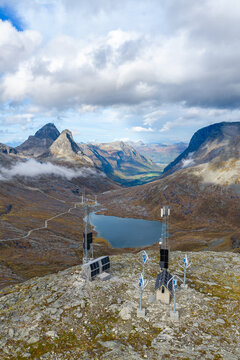 Aerial view of a remote power station with wind turbines and solar panels on a rocky mountain ridge overlooking a lake, Andalsnes, More og Romsdal, Norway.