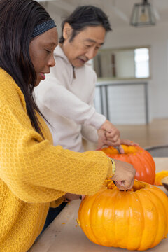 Diverse friends carving pumpkins at table African woman mustard sweater Senior man halloween