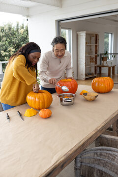 Senior Asian man and woman carving pumpkins scooping pulp into pot on porch halloween