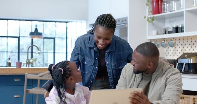 African family reacting to daughter gesturing, leaning, laughing while viewing laptop in kitchen