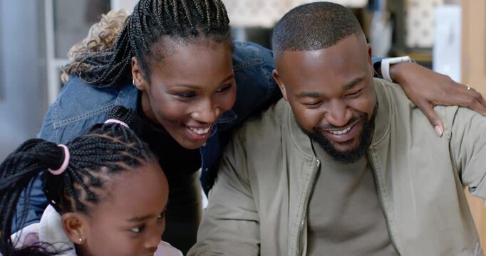 Parents and daughter leaning in, watching shared device in kitchen, reacting to screen and laughing