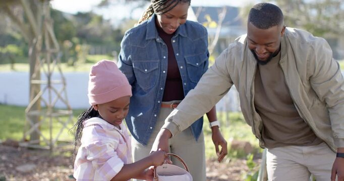 African family teaching child while watering garden beds, father guiding hand, pink watering can