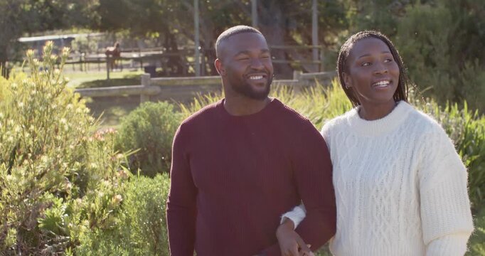 Couple walking linked, woman hooking arm through man's, scanning park, wearing knits