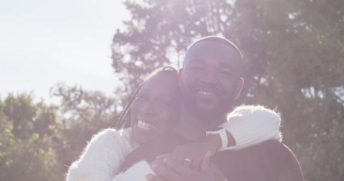 African American couple in park, woman approaching, hugging man, showing ring and watch