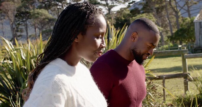 Couple walking grassy path, man in maroon knit glancing at woman in white knit, sparking laughter
