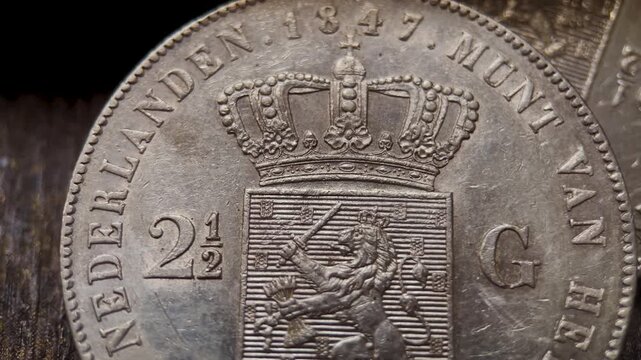 Macro video of the reverse side of an antique Dutch gulden coin, featuring a crowned heraldic shield, denomination mark, engraved lettering, and worn silver texture.
