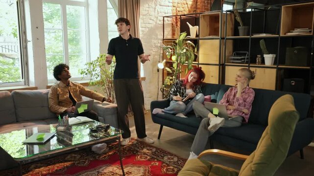 Standing colleague explains ideas to seated teammates in shared workspace with assertive energy. Team communication, conflict resolution, hybrid work concept