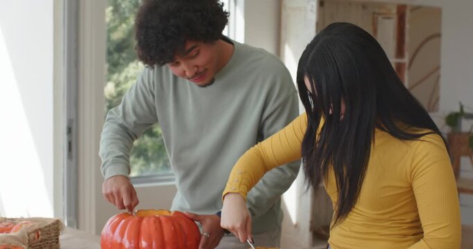 African American couple cutting lids, scooping pumpkin pulp into metal bowl on kraft for halloween