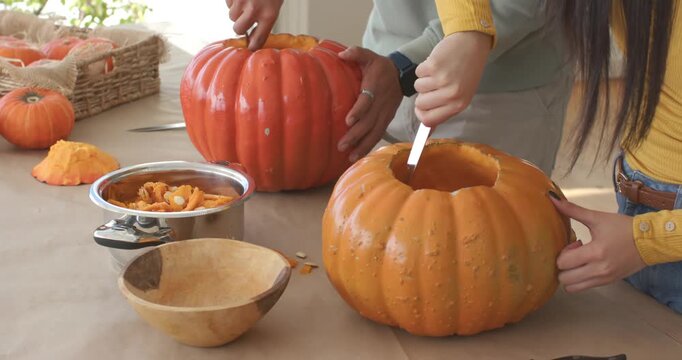 African American couple carving pumpkins cutting lids scooping pulp in bowl at table for halloween