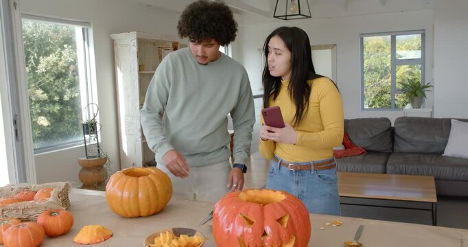African couple inspecting carved pumpkin after purple phone prompt, aligning for halloween selfie