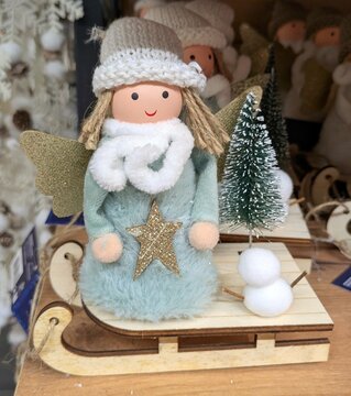 Decoraci&oacute;n de Navidad. Mu&ntilde;eco de un &aacute;ngel con alas doradas, con un sombrero de lana, bufanda y t&uacute;nica con una estrella, colocado sobre un trineo de madera con un &aacute;rbol de navidad