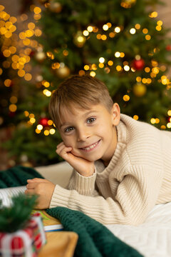Cute preschool boy, sitting in front of the fireplace, holding christmas present and reading a book, joy and happiness