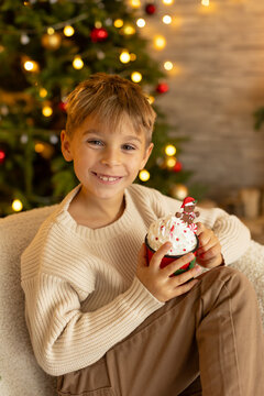 Cute preschool boy, sitting in front of the fireplace, holding christmas present and reading a book, joy and happiness