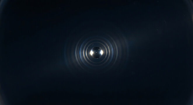 Optical tweezers laser trap holding a microscopic silica microsphere suspended in pure water with diffraction rings and darkfield background