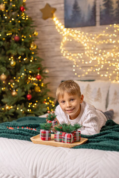 Cute preschool boy, sitting in front of the fireplace, holding christmas present and reading a book, joy and happiness